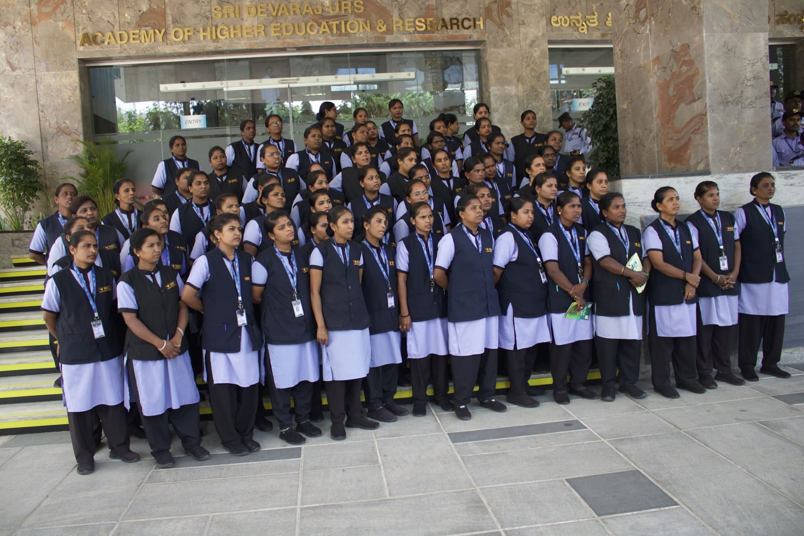 SDC lady guards in navy vests and guards in caps lined up on the steps outside an academy building